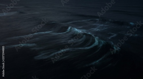 Bild auf Leinwand An aerial top-down view of abstract dark ocean waves swirling with bioluminescen