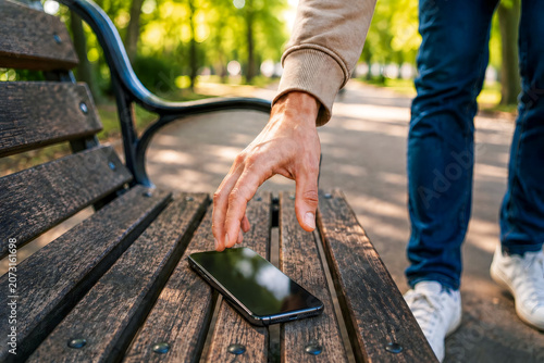 Man Reaching for Smartphone on Park Bench Outdoors