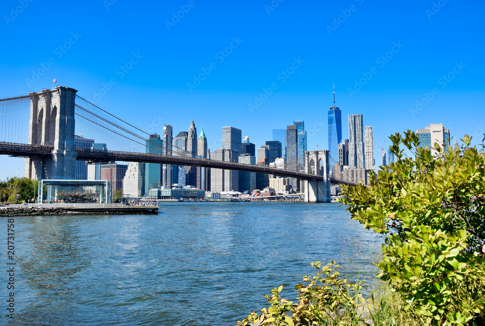 Obraz premium Brooklyn Bridge granite tower and sweeping span close-up from East River with One World Trade Center behind, New York City, USA