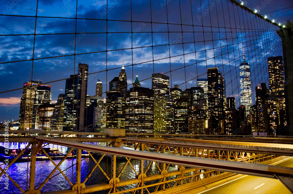 Obraz premium Lower Manhattan illuminated skyline with One World Trade Center seen through Brooklyn Bridge steel cables and truss structure at dusk, New York City, USA