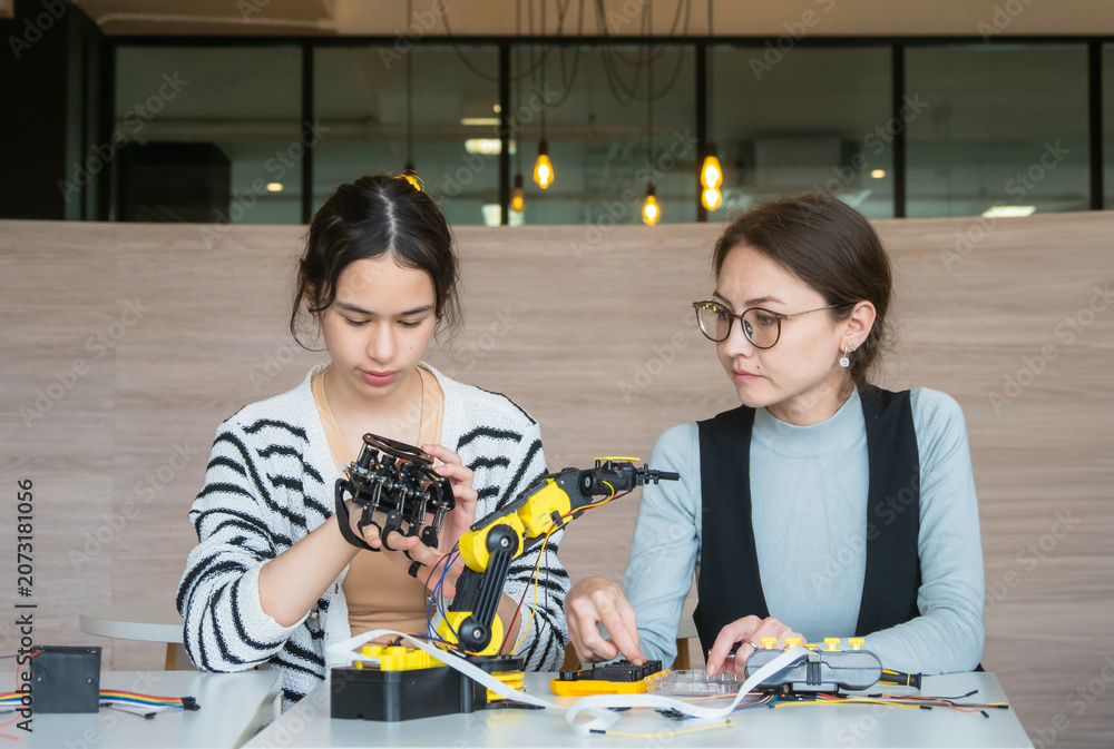Fototapeta premium Expert female mentor teaching young student robotic coding on laptop; diverse women collaborating on STEM education project fostering future innovation and learning modern classroom setting.