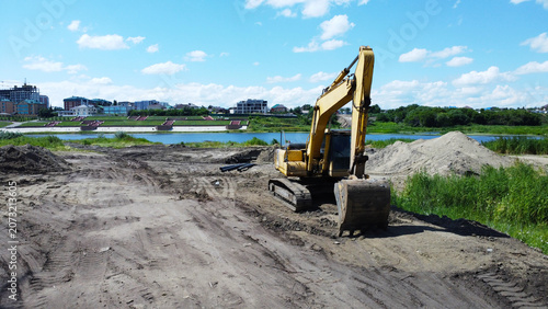 Photos Large yellow crawler excavator at an urban riverfront embankment construction si
