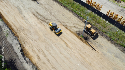 Fotografie Yellow road roller compacting a dirt road bed at an infrastructure construction