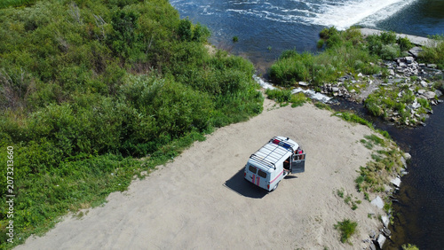Foto Aerial drone view of a camper van parked on a sandy riverbank near a water weir