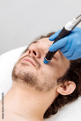 Professional facial skincare procedure with HydraFacial device for male client. Concept skin cleansing, hydration and aesthetic medicine.
