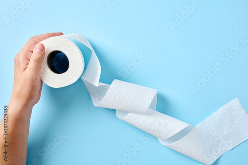 Schilderij op canvas A hand unrolling a long, wavy strip of white toilet paper across a bright blue surface