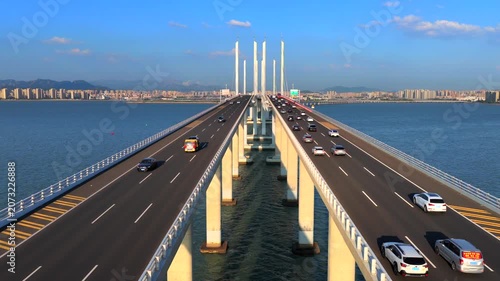An aerial view of the spectacular Jiaozhou Bay Bridge in Qingdao, Shandong, China, showing a busy cross-sea bridge with vehicles traveling across it.