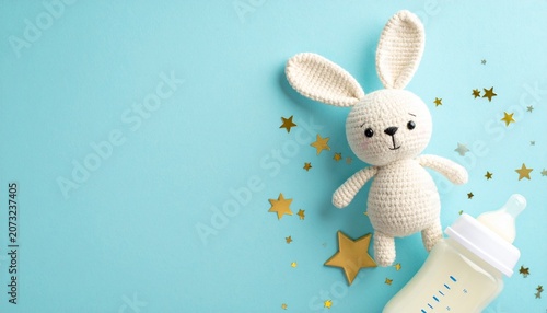 Top view photo of knitted bunny toy milk bottle and gold stars on isolated pastel blue background with copyspace