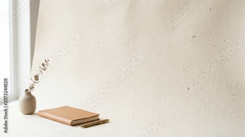 Minimalist workspace with closed notebook and dried plant in vase, notebook