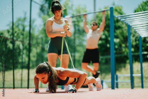 Obraz na płótnie A fit woman performs push-ups with a resistance band while teammates work out in the background