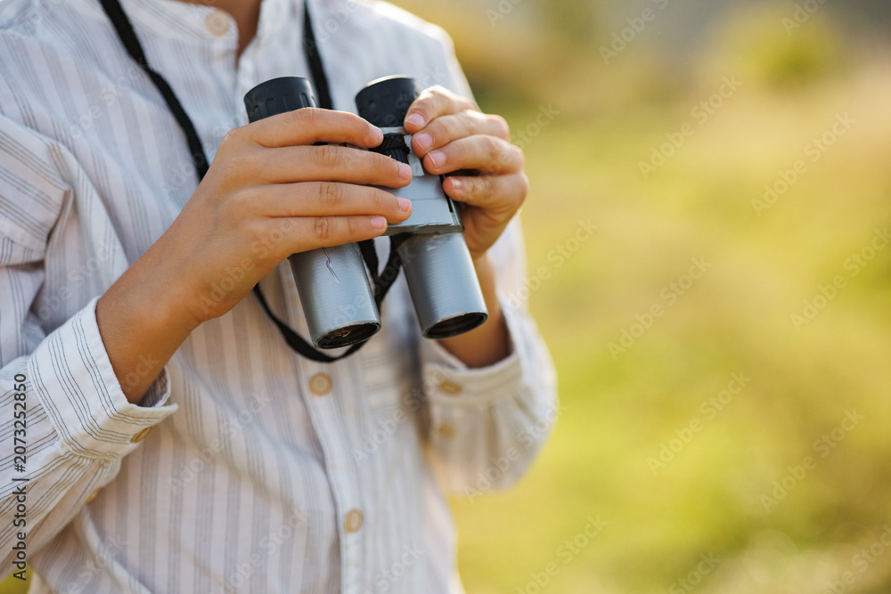 Fototapeta premium Midsection of a little boy standing in a field with a binoculars at summer