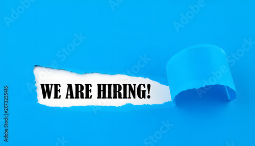 We Are Hiring Message Revealed Through Torn Blue Paper For Recruitment Career Opportunity And Human Resources Concept