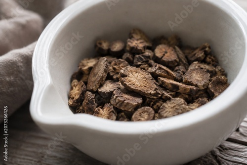 Dried slices of valerian root scattered in a white ceramic mortar with soft natural side lighting.