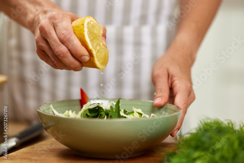 Person preparing a nutritious meal, adding fresh lemon juice to a bowl of vegetables, emphasizing healthy eating and cooking