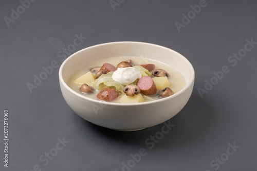 Kapustnica in white bowl, filled with creamy soup, topped with sliced mushrooms, cabbage, and sour cream. Concept of cabbage soup with sausage mushrooms cream.