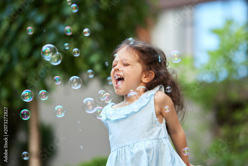 Girl closing eyes and laughing aloud while playing outdoors, enjoying a moment of childhood joy and summer happiness