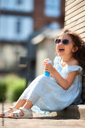 Happy child wearing sunglasses and summer dress, enjoying play with bubbles in bright sunshine, feeling pure joy of childhood days