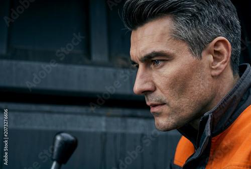 High-concentration profile portrait of a male operator. Rembrandt lighting defines cheekbone structure, steel-gray eye in sharp focus, vellus hair, realistic skin texture, and uniform fabric.

