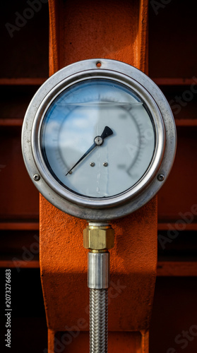  professional technical still life close up oblique focus on industrial hydraulic pressure gauge assembly. hard side raking light highlights structural depth and bracket micro relief.

