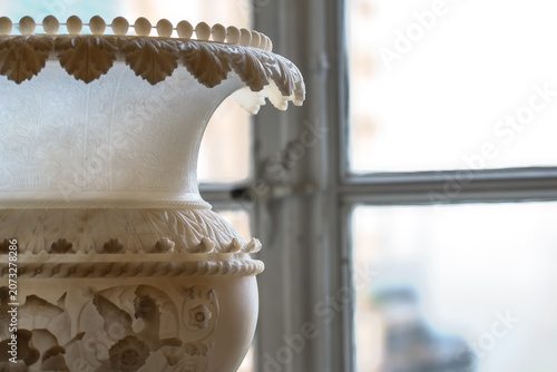 An intricately carved alabaster vase is prominently displayed in the foreground, its detailed ornamentation highlighted by soft, diffused light filtering through a nearby window
