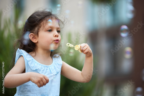 Preschooler child having fun outdoors, blowing soap bubbles, enjoying childhood innocence and playful activity in summer