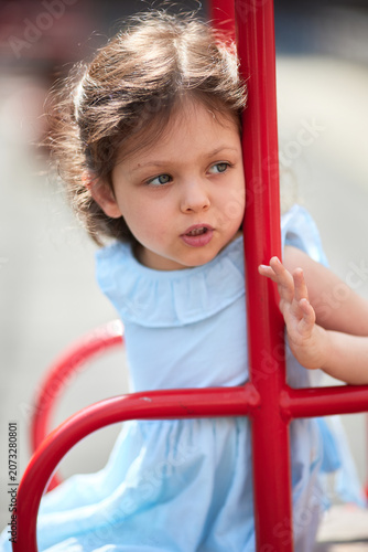 Child girl is swinging on a red swing set, enjoying childhood during summer