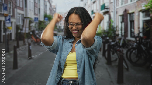 Valokuva Woman with clenched fists and open mouth cheering on a street lined with bicycles and rowhouses; triumph elation