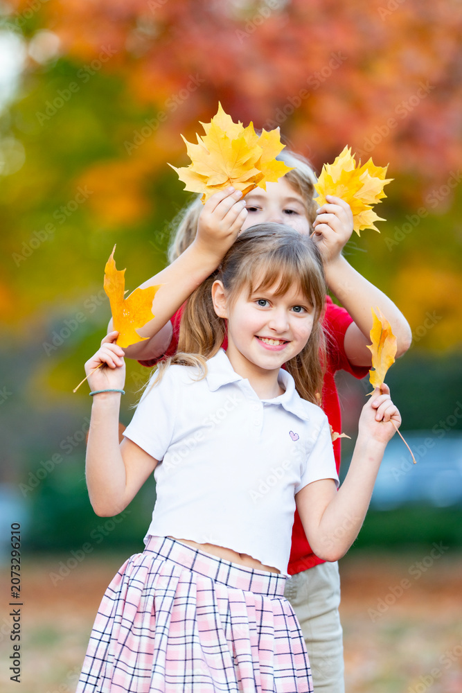 Fototapeta premium Friends kids enjoy autumn leaves. Friends children smile in autumn park. Friends kids hold colorful autumn foliage. Friends children share happy autumn fun.