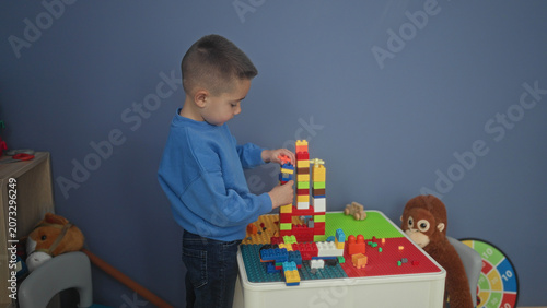Fotografía Hispanic boy carefully stacking colorful plastic blocks with hands into a tall tower on a play table in building; quiet concentration