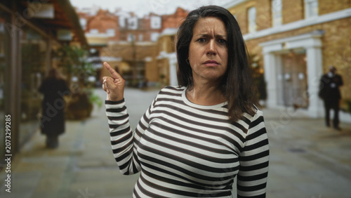 фотографія Woman points finger toward shopfront on street, bare finger visible and striped sweater prominent; disapproval warning