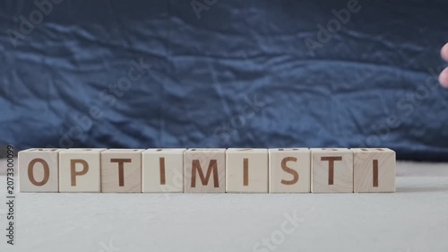 motivational word optimistic !, laying out  by hand from letters on wooden cubes, slow motion
