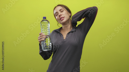 Photos Woman holding large plastic water bottle with closed eyes, hand on neck and slight grimace in studio; relief rest recovery