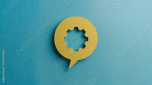 Yellow paper speech bubble with gear cutout on blue background symbolizing technical support communication