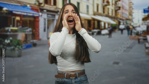 Foto Young woman cupping hands at mouth shouting on a lively pedestrian street lined with shops, awnings and planters; cheering joy