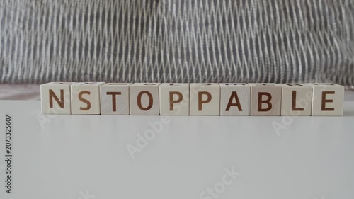 motivational word unstoppable, laying out  by hand from letters on wooden cubes, slow motion
