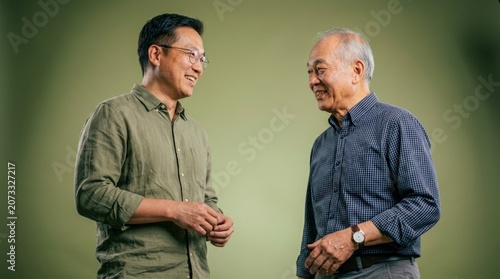 Two men of Asian descent, one younger and one older, are engaged in a conversation, smiling warmly at each other.