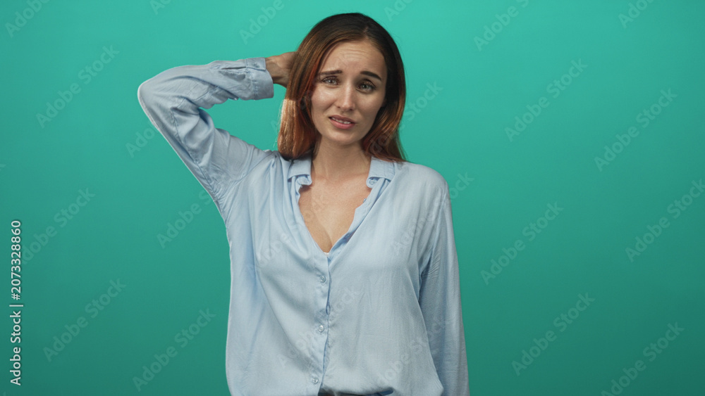 Fototapeta premium Redhead woman with hand behind head, furrowed brow, slightly exposed neckline and puzzled expression in studio; confusion.