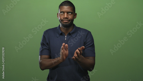 Man clapping hands with an eye roll and sardonic expression, navy polo visible in green studio setting; dry sarcasm.