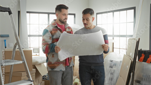 Photos Man holding blueprint with both hands and reading plan in an apartment full of boxes and ladder; home planning anticipation
