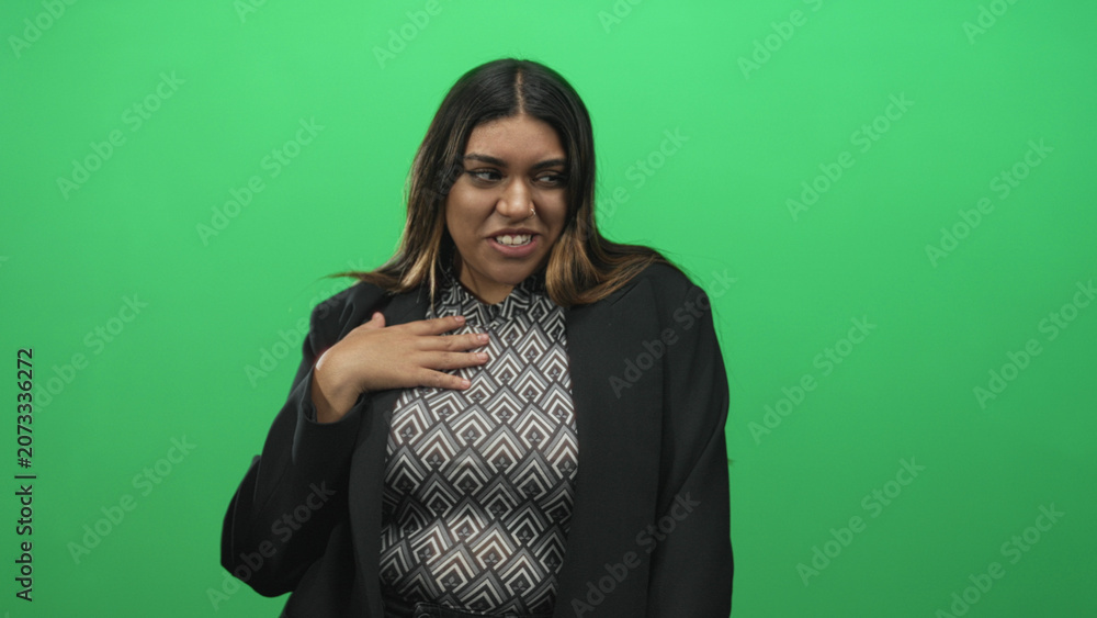 Fototapeta premium Woman touching hand to chest in green screen studio wearing patterned top and blazer; shyness authenticity.