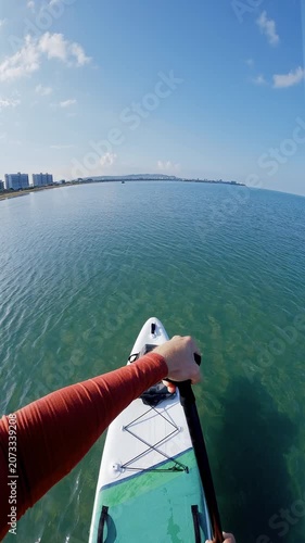 First person view on stand up paddle board gliding over turquoise ocean near coastal city buildings