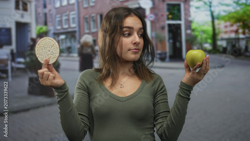 Foto Woman holds green apple in one hand and rice cake in the other on a cobbled city street while weighing options; indecision