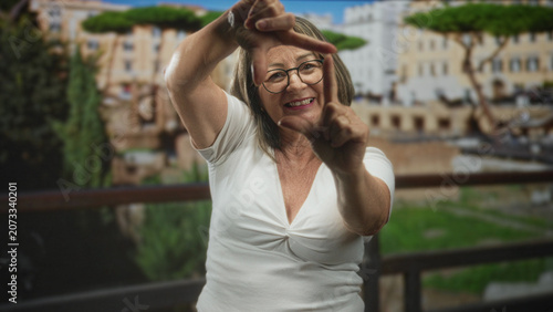 Konstfotografi Woman frames the view with her fingers and smiles, bare hands and forearms visible on a balcony beside a building; playful joy
