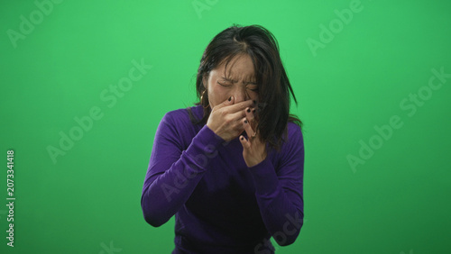 Obraz na plátně Woman with hand covering mouth and other hand clutching her throat while coughing and gagging against a green studio backdrop; distress illness