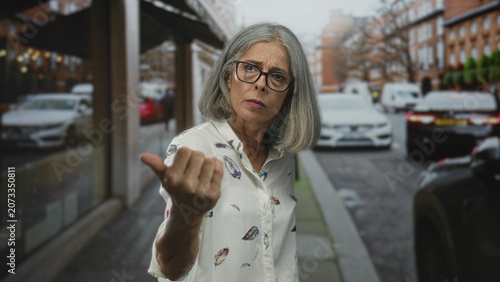 Fotografie Woman points finger forward on street wearing glasses and patterned blouse with stern expression; anger
