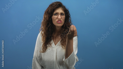 Schilderij op canvas Woman with beckoning hand gesture and tense facial expression in studio against blue backdrop; annoyance impatience