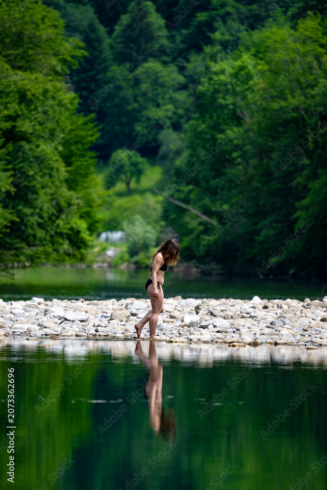 Fototapeta premium Woman enjoying a tranquil moment beside emerald waters of the Kupa River, highlighting sustainable holidays, mindfulness and authentic rural experiences