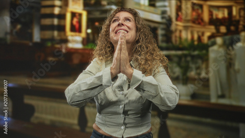 Foto Woman with hands clasped in prayer, palms together and face uplifted, curly hair visible and bare hands held near chest inside church building; devotion hope relief