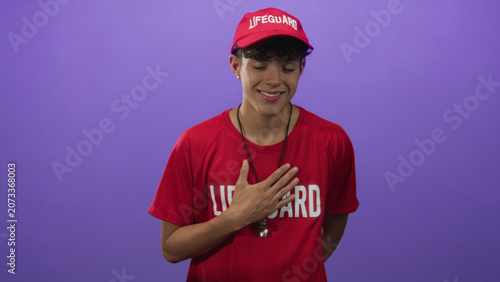 Fotografía Lifeguard teenager with hand on chest, red cap and whistle visible, posing with eyes closed in studio; sincerity duty