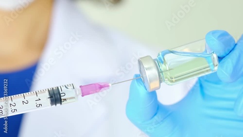 Health and medical concepts close up shot with unrecognizable doctor hand holding syringe and blue vaccine bottle at hospital in 4K Ultra HD footage.
